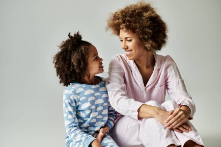 Téléchargez les photos : A happy African American mother and daughter in pajamas sitting on the floor together in a cozy setting. - en image libre de droit