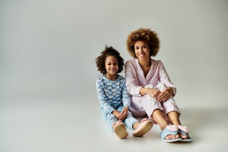 Foto de Una madre e hija afroamericana felizmente sentadas en el suelo en pijama, disfrutando de un momento acogedor juntas. - Imagen libre de derechos