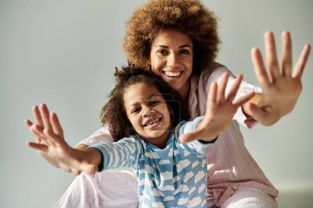 Une heureuse mère et fille afro-américaine en pyjama posant ensemble sur un fond gris.
