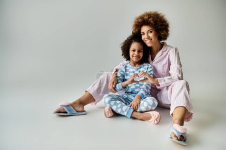 Foto de Alegre madre e hija afroamericana sentadas de cerca en el suelo en pijamas a juego, compartiendo un momento especial. - Imagen libre de derechos