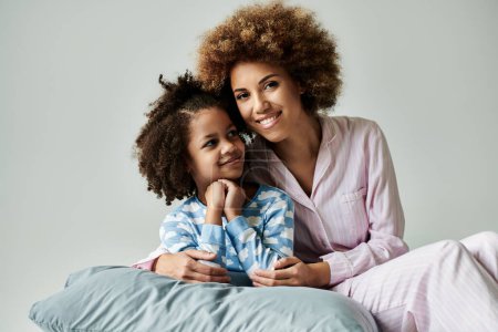 Foto de An African American mother and daughter in pajamas happily posing for a photo on a grey background. - Imagen libre de derechos