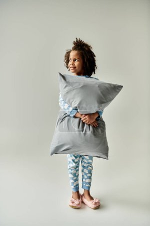 A little girl in pajamas cuddling a grey pillow. Cozy vibes ensue.