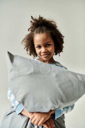 A young girl joyfully hugging a fluffy pillow against a serene white backdrop.