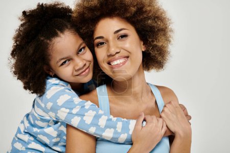 Téléchargez les photos : Une heureuse mère et fille afro-américaine en pyjama posant ensemble sur un fond gris. - en image libre de droit