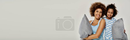 Photo for Two women in pajamas strike playful poses with pillows against a white backdrop. - Royalty Free Image