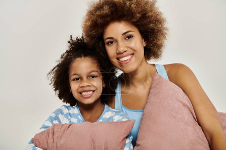 Happy African American mother and daughter smiling in pajamas while posing together on a grey background.