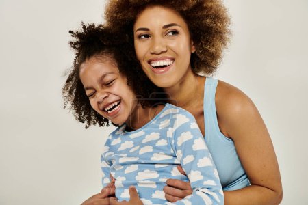 Photo for A happy African American mother wearing pajamas hugging her daughter tenderly in front of a white background. - Royalty Free Image