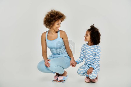 Foto de Una madre y una hija afroamericanas felices en pijamas a juego, compartiendo un momento alegre sobre un fondo blanco. - Imagen libre de derechos