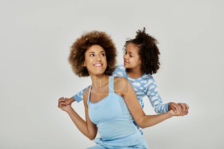 Foto de Una madre y una hija afroamericanas felices en pijama posan con gracia frente a un fondo gris. - Imagen libre de derechos