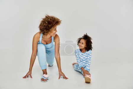 Photo for Joyful African American mother and daughter in pajamas practicing yoga together on a peaceful white background. - Royalty Free Image