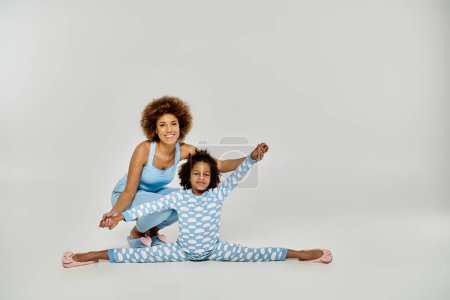 Photo for A happy African American mother and daughter in pajamas practicing yoga together on a white background. - Royalty Free Image