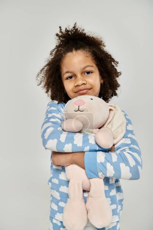 Ein afroamerikanisches Mädchen im Schlafanzug hält freudig ein Stofftier in der Hand