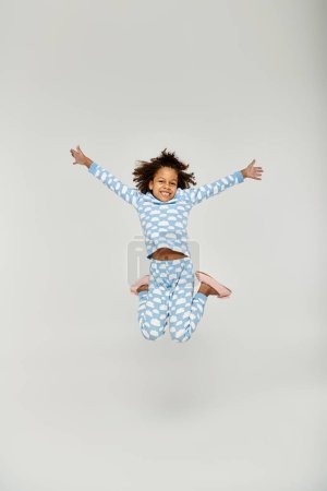 Una joven afroamericana saltando alegremente en el aire, usando pijamas azules