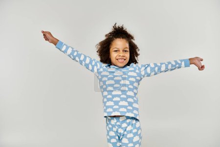 Joven afroamericana en pijama azul extiende los brazos, expresando alegría y libertad