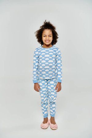Feliz madre e hija afroamericana en pijamas de lunares azules y blancos a juego sobre un fondo gris.