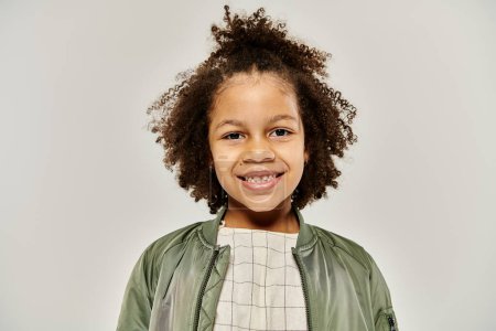 Téléchargez les photos : Un enfant afro-américain frisé en vêtements élégants portant une veste de bombardier verte. - en image libre de droit