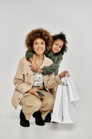 A stylish curly African American mother and son holding shopping bags on a white background.