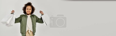 Téléchargez les photos : A young boy confidently holds shopping bags in front of a white background. - en image libre de droit