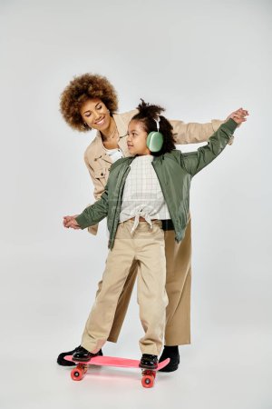 Foto de La madre y la hija afroamericanas rizadas con ropa elegante patinan juntas con confianza sobre un fondo gris. - Imagen libre de derechos