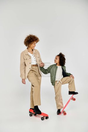 A curly African American mother and daughter, both in stylish clothes, standing confidently on a skateboard against a grey background.