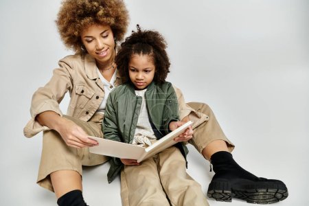 Eine lockige afroamerikanische Mutter und ihre Tochter sitzen auf dem Boden, in ein Buch vertieft, und teilen einen besonderen Moment des gemeinsamen Lesens.