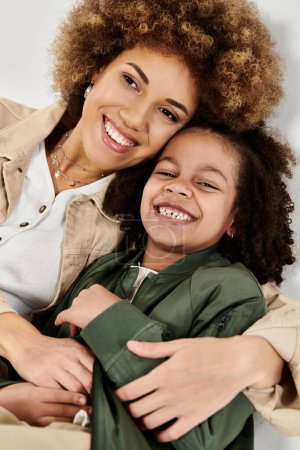 Foto de Rizado afroamericano madre e hija en ropa elegante abrazándose unos a otros sobre un fondo blanco. - Imagen libre de derechos