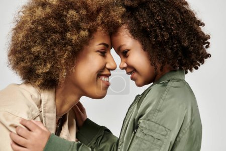 Téléchargez les photos : Une mère et une fille afro-américaines frisées, vêtues de vêtements élégants, partagent un câlin sincère sur un fond blanc. - en image libre de droit