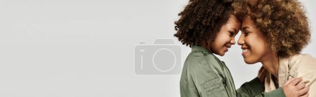 Foto de Dos mujeres afroamericanas rizadas con un atuendo elegante abrazándose tiernamente contra un fondo blanco. - Imagen libre de derechos