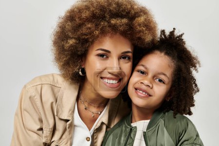 Foto de Una elegante madre afroamericana con el pelo rizado afro y su niña posando sobre un fondo gris. - Imagen libre de derechos
