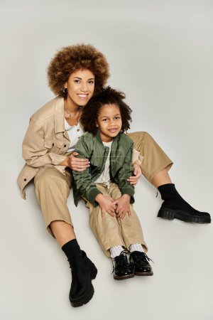 Téléchargez les photos : Curly afro-américaine mère et fille dans des vêtements élégants posent élégamment sur un fond gris. - en image libre de droit