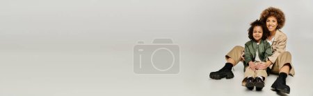 Photo for Curly African American mother and daughter sitting together in stylish clothes on a grey background. - Royalty Free Image