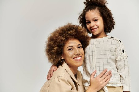 Photo for Curly African American mother and daughter in fashionable attire, striking a pose together on a chic grey backdrop. - Royalty Free Image