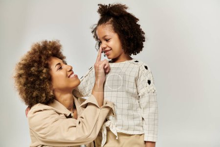 Eine lockige afroamerikanische Mutter und ihre Tochter in stilvollen Kleidern teilen einen zarten Moment und berühren die Nase