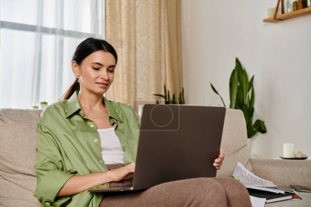 Woman in casual attire on a couch using laptop.