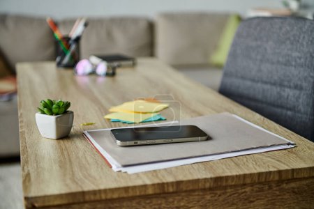 Wooden table with cell phone next to potted plant.