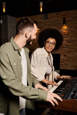 Un hombre y una mujer de pie junto a un teclado en un estudio de grabación, inmersos en la creación de música para su ensayo de la banda.
