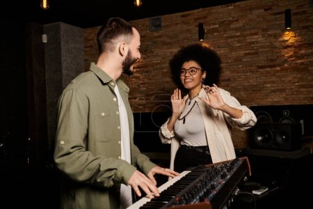 Un hombre y una mujer colaboran junto a un teclado en un estudio de grabación durante una sesión de ensayo de la banda de música.
