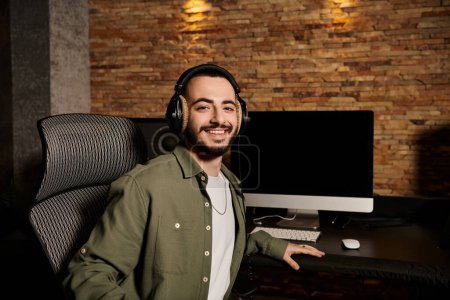 A man in a green shirt smiles as he works on a computer in a recording studio during a music band rehearsal.