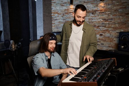 Two men in a recording studio, deeply engrossed, playing a keyboard together during a music band rehearsal.
