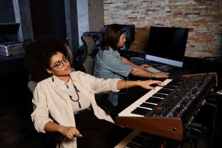 Foto de Dos músicos están sentados en un estudio de grabación, trabajando juntos en un teclado, ensayando para su actuación en la banda de música. - Imagen libre de derechos