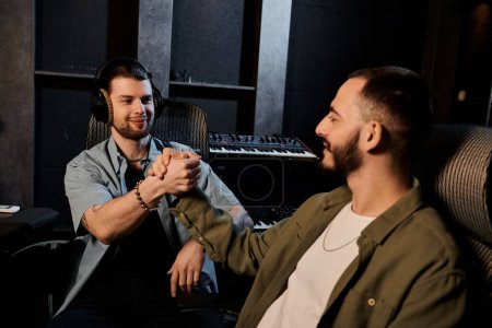 Two men in a recording studio, one wearing headphones, shaking hands in agreement during a music band rehearsal.
