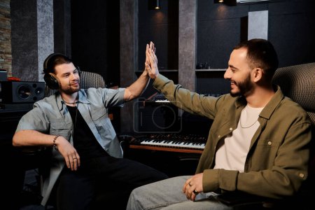 Two men in a recording studio, members of a music band, celebrating with high fives after a successful rehearsal session.
