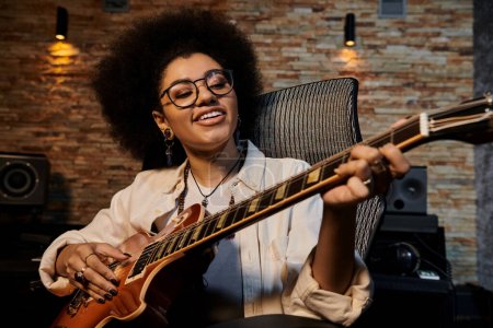Photo for A woman with glasses strums a guitar in a recording studio during a music band rehearsal. - Royalty Free Image