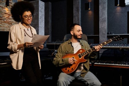 A man and woman playing guitar in a recording studio during a music band rehearsal.
