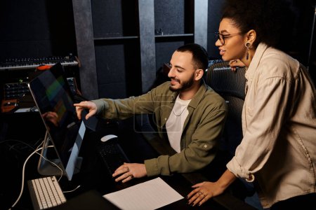 A man and woman collaborate on a computer in a recording studio during a music band rehearsal.