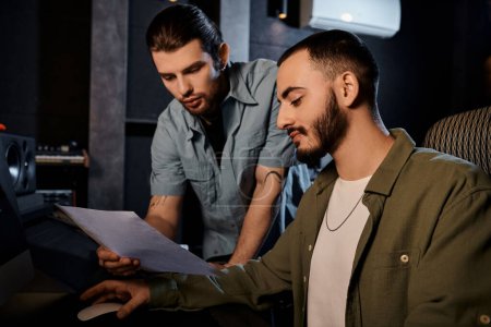 Two men in a recording studio carefully analyze a sheet of notes, deep in discussion.