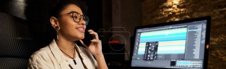 Photo for A woman multitasks, talking on the phone while sitting in front of a computer during a music band rehearsal in a recording studio. - Royalty Free Image