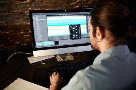 Ein Mann, der am Computer Musik komponiert und sich auf die Aufgabe vor einem großen Monitor konzentriert.