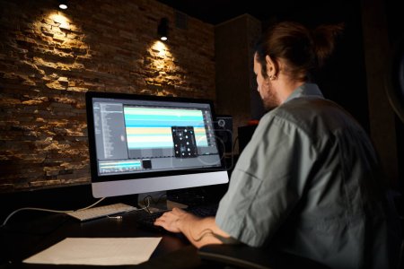 Ein Mann, der sich in die Arbeit am Computer vertieft und während einer Bandprobe in einem professionellen Tonstudio Musik macht.