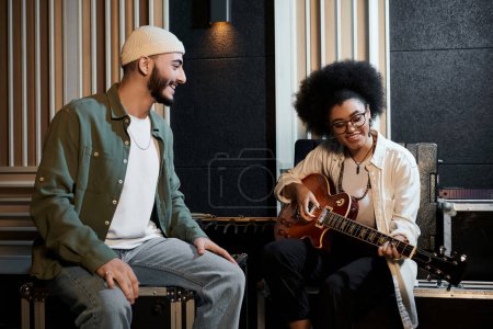 A man and a woman play guitar in a recording studio, creating music together as they rehearse for their band.